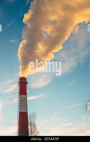 Der hohe Schornstein des Kesselraums im Frost gegen die Himmel mit gelbem Rauch - Heizperiode Stockfoto