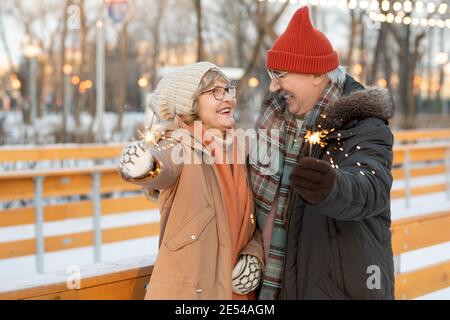 Glückliches reifes Paar, das Wunderkerzen hält und sich lächelt Sie feiern Weihnachten im Park Stockfoto
