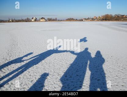 Schatten im Schnee einer unwiedererkennbaren, fröhlichen und freundlichen Familie. Vier Hände halten. Eltern, Kinder und ein Hund. Aktiver Lebensstil, zu Fuß. Sonniger Wintertag Stockfoto