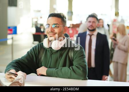 Junger Mann in Brillen, der an der Rezeption stand und vor dem Check-in eincheckte Flug mit Menschen hinter ihm im Hintergrund stehen Stockfoto