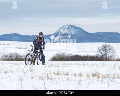 Biker schiebt Fahrrad allein im Tiefschnee. MTB-Fahrer verlor die Straße unter Schnee. Kalter Wintertag, Hügel am Horizont Stockfoto