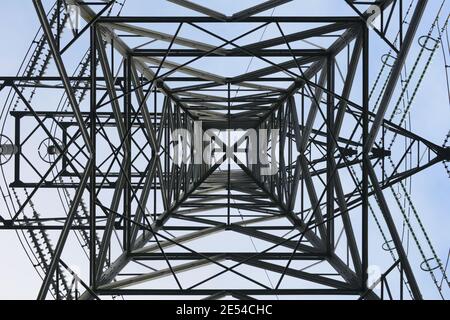 Elektrischer Pylon von direkt darunter mit blauem Himmel über dem Kopf, vertikale Symmetrie, nach oben Stockfoto