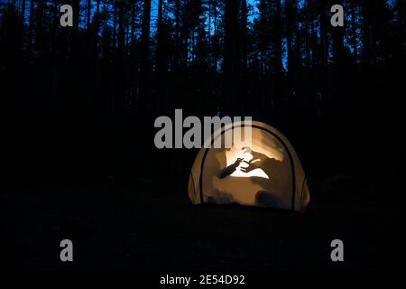 Silhouetten von Kindern, die nachts im Zelt spielen, machen Schattenpuppen mit Taschenlampe und genießen Sommerferien Stockfoto