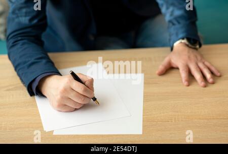 Geschäftsmann im Büro schreibt einen Brief oder unterzeichnet ein Dokument auf einem Stück weißem Papier mit einem Brunnen Stift mit Spitze Stockfoto