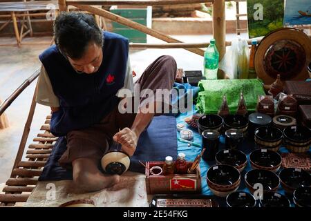 Ein burmesischer Handwerker malt eine Schale mit einem Fuß in einem Straßenstand, Inle Lake, Myanmar. Stockfoto