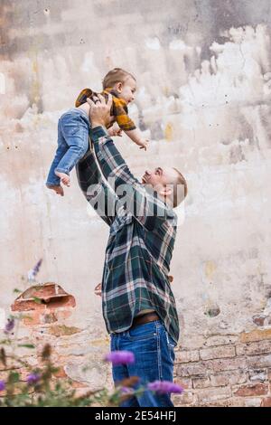 Ein Vater und sein Baby Sohn draußen in einer Stadt Einstellung gegen eine alte strukturierte Wand Stockfoto