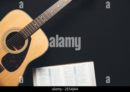 Eine Gitarre und eine offene bibel auf schwarzem Hintergrund In einer schwach beleuchteten Umgebung Stockfoto