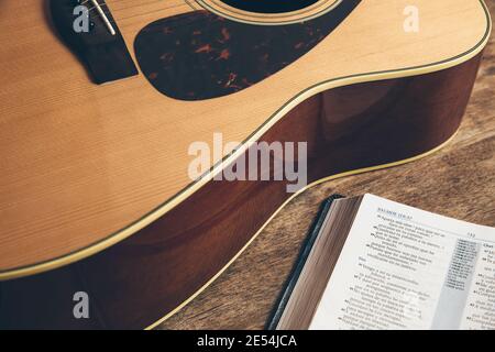 Seitenansicht einer Gitarre und einer offenen bibel auf Ein Holzhintergrund in einer schwach beleuchteten Umgebung Stockfoto