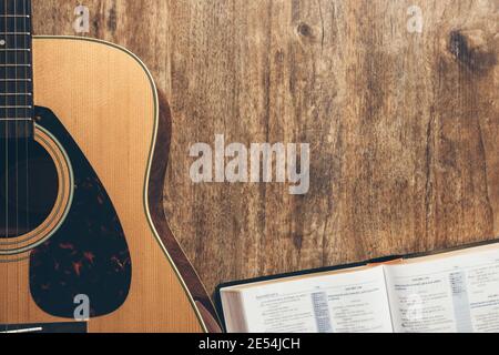 Eine Gitarre und eine offene bibel auf einem hölzernen Hintergrund In einer schwach beleuchteten Umgebung Stockfoto