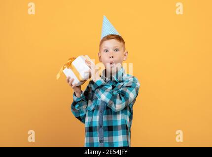 Aufgeregt Ingwer Junge in Papierkappe hält Geschenkbox Stockfoto