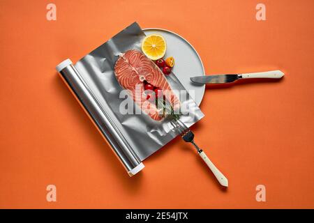 Frischer Lachs mit Zitrone in Folienpapier, fertig zum Kochen im Ofen auf orangefarbenem Hintergrund. Stockfoto