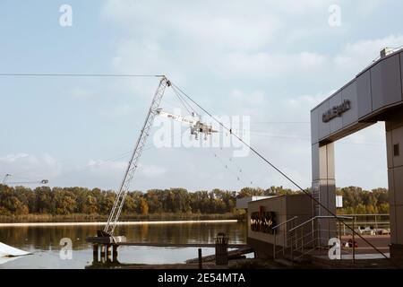 Installationsarbeiten am Cable Park am Ufer des Dnipro-Flusses, Arbeiter-Kletterer hängen am Kran unter Wasser am Himmel Hintergrund Stockfoto