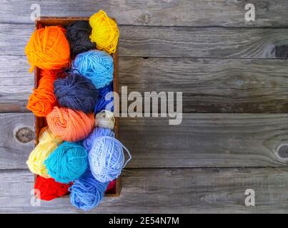 Kugeln aus hellem Wollgarn in einer Holzkiste auf altem Holzhintergrund. Stockfoto