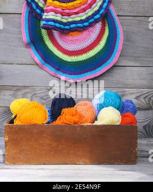 Gestrickte bunt gestreifte Matten und Bälle aus hellem Wollgarn in einer Holzkiste auf altem Holz-Wandhintergrund. Stockfoto