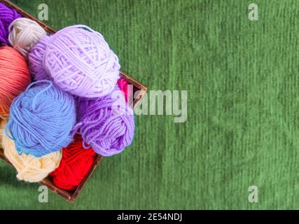 Kugeln aus buntem Wollgarn in einer Holzkiste auf grünem Strickhintergrund. Stockfoto