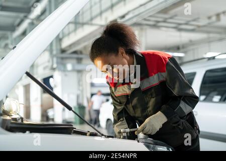 Junge Arbeiterin der Kfz-Reparatur-Service Biegen über offen Motorraum und Suche nach dem Grund für den Ausfall in Werkstatt Stockfoto