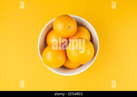 Direkt über der Ansicht der weißen Schüssel mit saftigen Orangen gefüllt Auf orangefarbenem Hintergrund Stockfoto