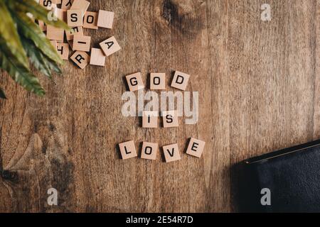 Gott ist Liebe, die in Blockbuchstaben auf einem Holztisch mit einer bibel und einer Pflanze geschrieben ist. Stockfoto