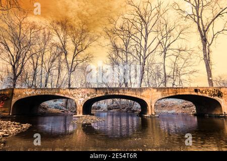 Eine dreibogenige Betonbrücke mit vielen Graffiti, die Guthrie Creek im westlichen Jackson County Indiana überspannt. Falschfarben-Infrarot-Iamge. Stockfoto