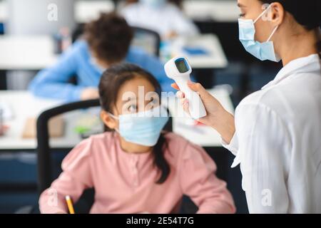 Lehrer mit kontaktlosen Thermometer Messung der Temperatur der asiatischen Mädchen Stockfoto