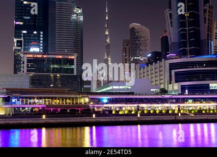 Blick auf den Burj khalifa umgeben von Gebäuden und Hotels Blick auf den farbenfroh beleuchteten dubai Canal Boardwalk Waterfall in Dubai Stockfoto