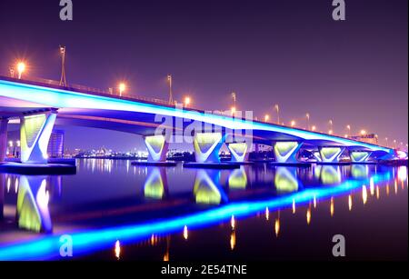 Schöne Winternachtsansicht der blau beleuchteten Al Garhoud Brücke in Dubai, Vereinigte Arabische Emirate mit der bunten Reflexion auf dem Wasser. Stockfoto