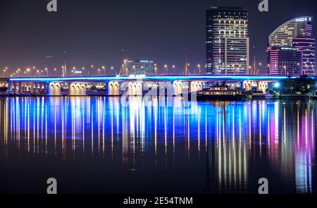 Wunderschöner Blick über Nacht auf die beleuchtete Business Bay Brücke über die Wasser mit Reflexen umgeben von den majestätischen Wolkenkratzern eingefangen In Dubai Stockfoto