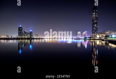 Wunderschöner Blick über Nacht auf die beleuchtete Business Bay Brücke über die Wasser mit Reflexen umgeben von den majestätischen Wolkenkratzern eingefangen In Dubai Stockfoto