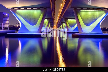 Schöne Winternachtsansicht der berühmten blau beleuchteten Al Garhoud Brücke in Dubai, Vereinigte Arabische Emirate mit der bunten Reflexion im Wasser Stockfoto