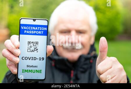 Älterer Mann, der einen Impfpass auf einem Mobiltelefon vorweist, was auf eine Impfung gegen covid-19 hinweist. Das Telefon zeigt einen nicht funktionsfähigen QR-Code an. Stockfoto