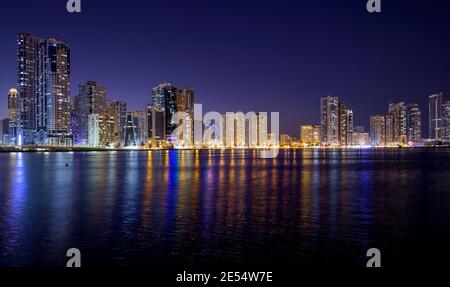 Panaromischer Blick auf den beleuchteten Himmel Scrappers zusammen mit Al Noor Moschee mit Reflexionen im Wasser gefangen bei der Al Majaz Waterfront Sharjah Stockfoto