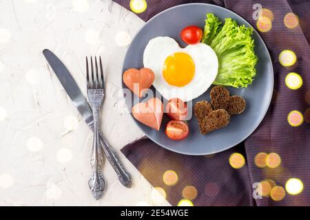 Valentinstag Frühstück mit herzförmigen Spiegelei serviert auf grauen Teller. Flach legen, Blick von oben mit Bokeh Stockfoto