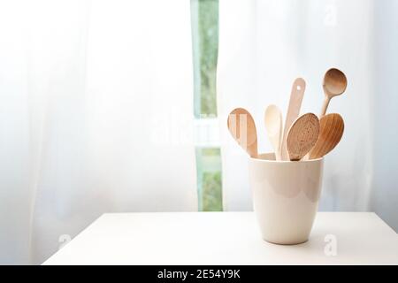 Keramiktopf mit Holzkochlöffel auf einem Tisch vor dem Küchenfenster mit weißen Vorhängen, Kopierraum, ausgewählter Fokus, enge Fieltiefe Stockfoto