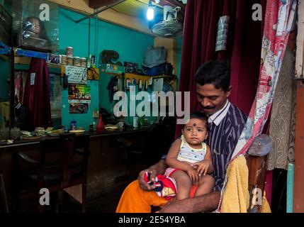 Tangalle, Sri Lanka: Barber sitzt vor seinem Laden mit seinem kleinen Sohn auf den Beinen Stockfoto