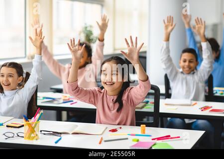 Diverse kleine Schüler, die im Klassenzimmer die Hände heben Stockfoto