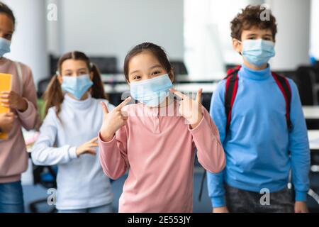 Asiatische Mädchen in medizinische Maske zeigt auf ihr Gesicht Stockfoto