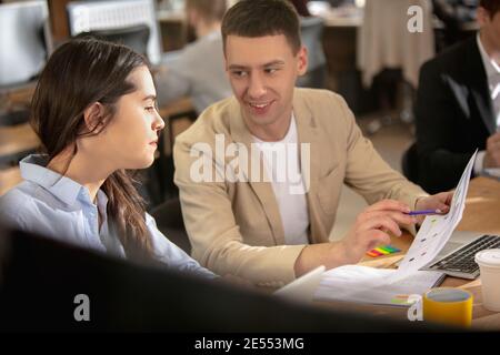 Reden, diskutieren. Junge kaukasische Kollegen arbeiten in einem Büro mit modernen Geräten und Gadgets zusammen. Schauen Sie beschäftigt, attened, fröhlich, erfolgreich. Konzept von Geschäft, Büro, Finanzen. Stockfoto
