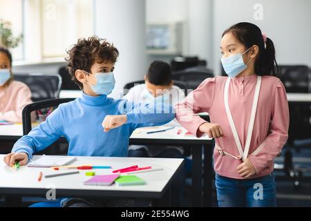 Kleine verschiedene Schüler tragen Gesichtsmasken Gruß und stoßen Ellbogen Stockfoto