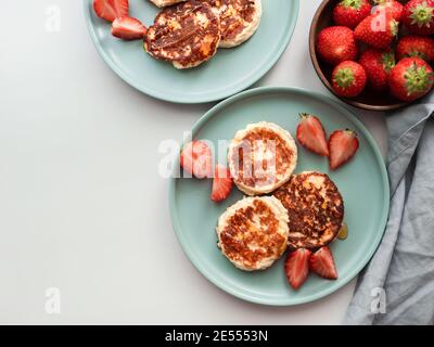Süße Käsepfannkuchen auf dem Teller serviert Erdbeeren. Quark Pfannkuchen, Syrniki, Ricotta Fritters, Quark Fritters. Ansicht von oben oder flach liegend. Platz für Text oder Design kopieren. Stockfoto