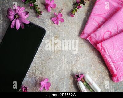 Frau Hygieneschutz während der Menstruation. Tampons aus Baumwolle, rosa Menstruationskissen, rosa Blüten und Smartphone auf Vintage-Tisch. Speicherplatz kopieren. Stockfoto