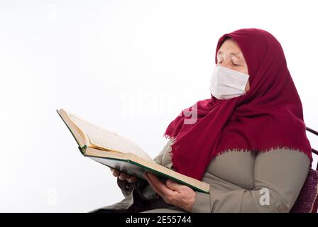 Alte türkische Frau trägt eine Maske. Muslimische Frau, die den Koran liest und eine Maske trägt Stockfoto