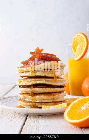 Pfannkuchenturm mit Orangenmarmelade, frischen Orangen und Saft zum Frühstück auf rustikalem Holztisch Stockfoto