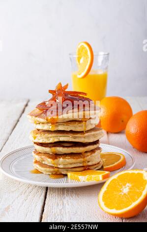 Pfannkuchenturm mit Orangenmarmelade, frischen Orangen und Saft zum Frühstück auf rustikalem Holztisch Stockfoto