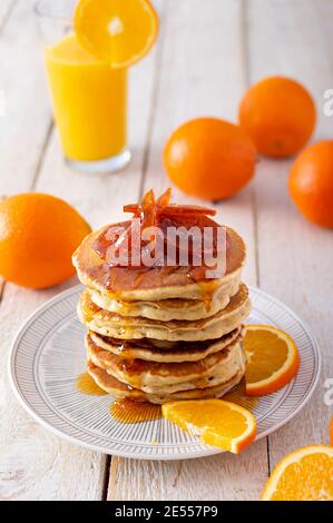 Pfannkuchenturm mit Orangenmarmelade, frischen Orangen und Saft zum Frühstück auf rustikalem Holztisch Stockfoto