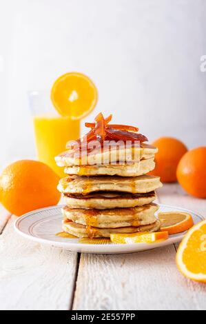 Pfannkuchenturm mit Orangenmarmelade, frischen Orangen und Saft zum Frühstück auf rustikalem Holztisch Stockfoto