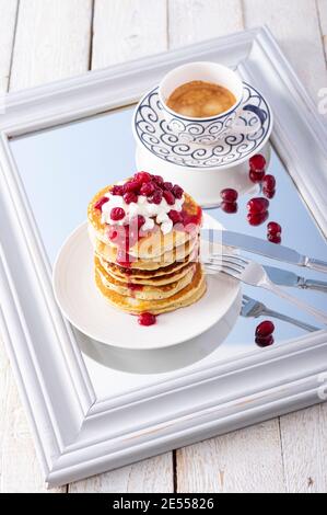 Pfannkuchenturm mit Cranberry-Marmelade, frischem Hüttenkäse und Kaffee zum Frühstück auf Spiegel über rustikalem Holztisch Stockfoto