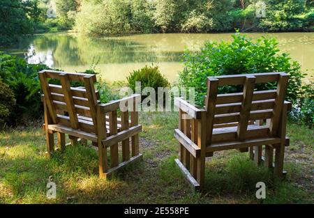 Friedliches Sitzen am Wasserrand. Zwei Gartenstühle blicken auf einen schönen grünen Teich. Ein Ort der Entspannung Stockfoto