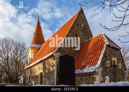 Prag, Tschechische Republik - Januar 13 2021: Gotische Steinkirche von Jakob dem Großen mit rotem Dach in Petrovice. Sonniger Wintertag mit blauem Himmel und Wolken. Stockfoto