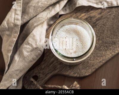 Weizensauerteig-Starter. Draufsicht des Glasgefäßes mit Sauerteig Starter auf Holzbrett. Platz für Text oder Design kopieren. Stockfoto