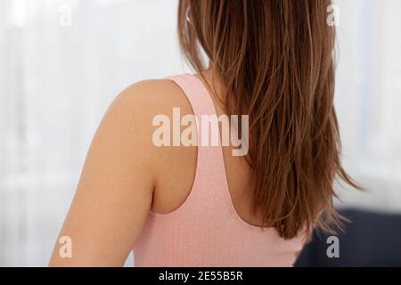 Nahaufnahme einer Frau mit langen braunen Haaren In einem rosa Sporttop auf einem Fensterhintergrund Stockfoto